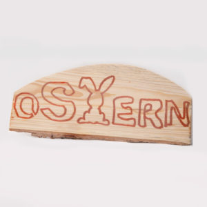 Holzstück mit eingraviertem Schriftzug 'OSTERN' und einem Hasenmotiv.